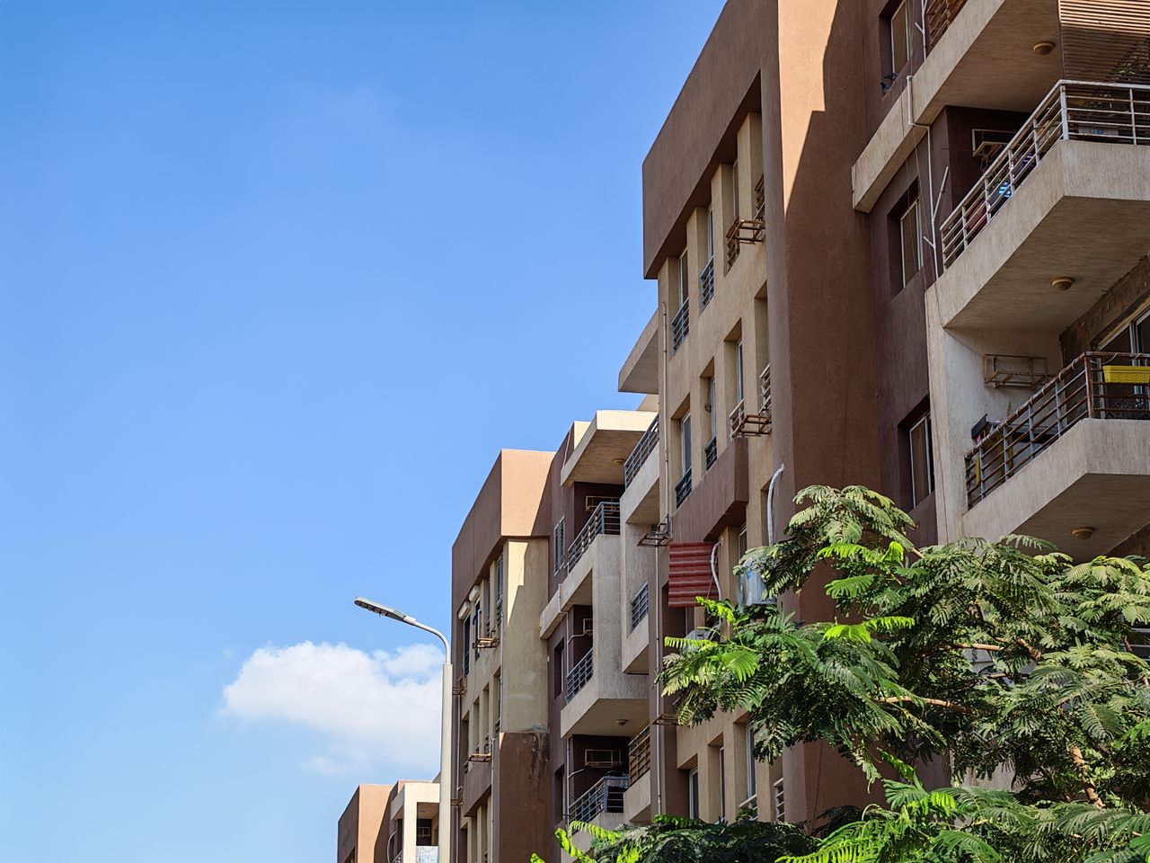 services-02 Urban apartment building against a bright blue sky with foliage in the foreground.